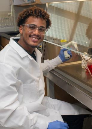 A student researcher smiles while holding lab equipment