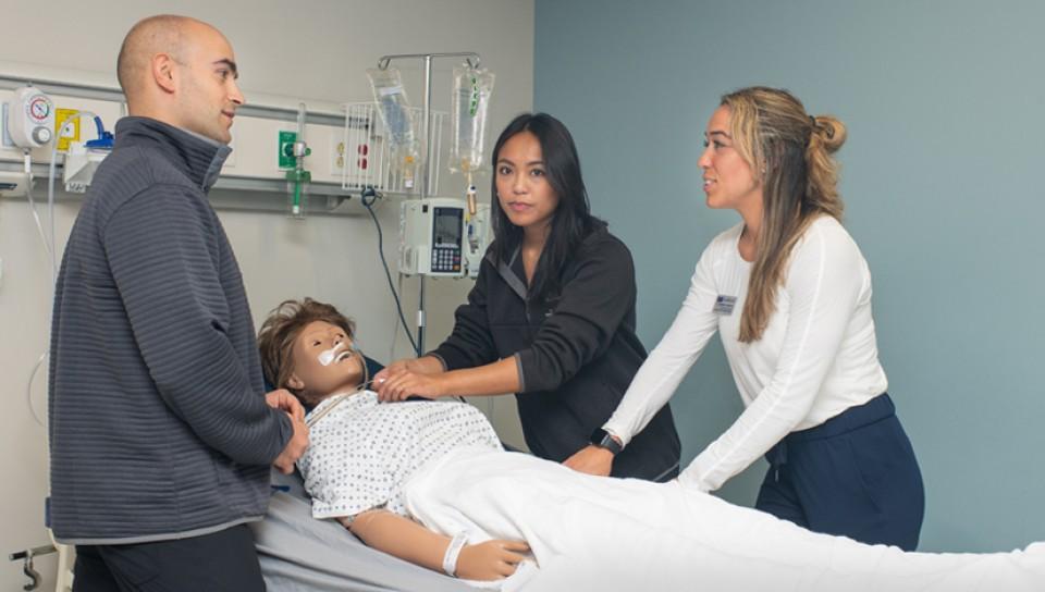 Three physical therapy students practicing on a dummy in the Simulation Lab
